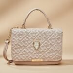 small, light pink or beige faux leather crossbody and top handle bag with a geometric pattern and gold-tone hardware.